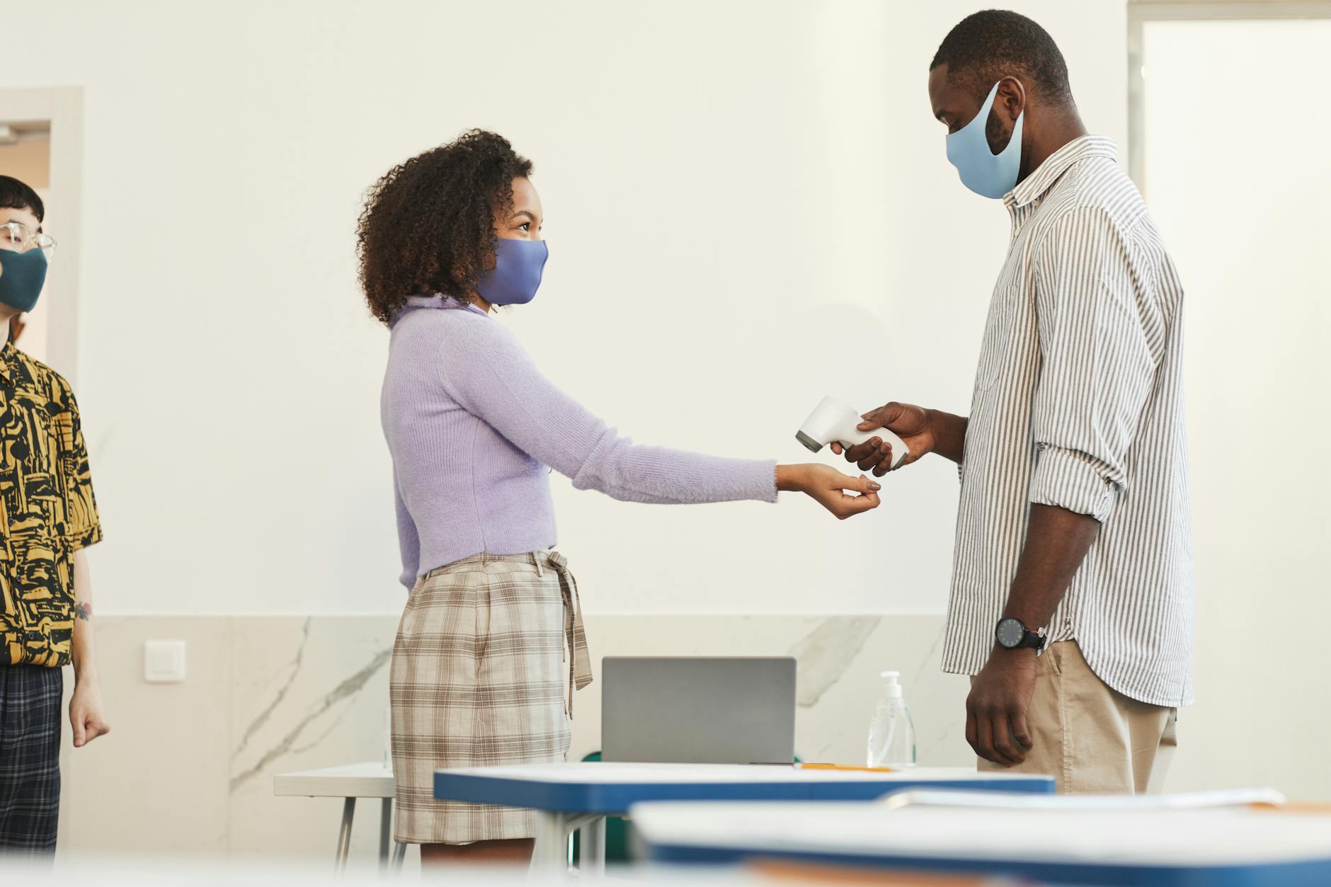 Nauczyciel mierzy temperaturę uczniowi termometrem bezdotykowym w klasie