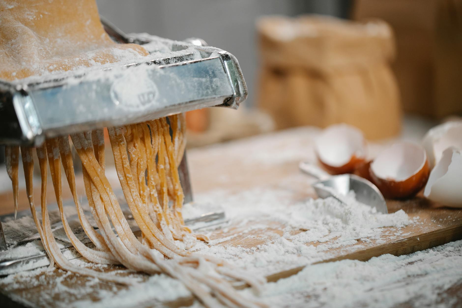 Świeże spaghetti z maszynki na drewnianym blacie z mąką i skorupkami jaj
