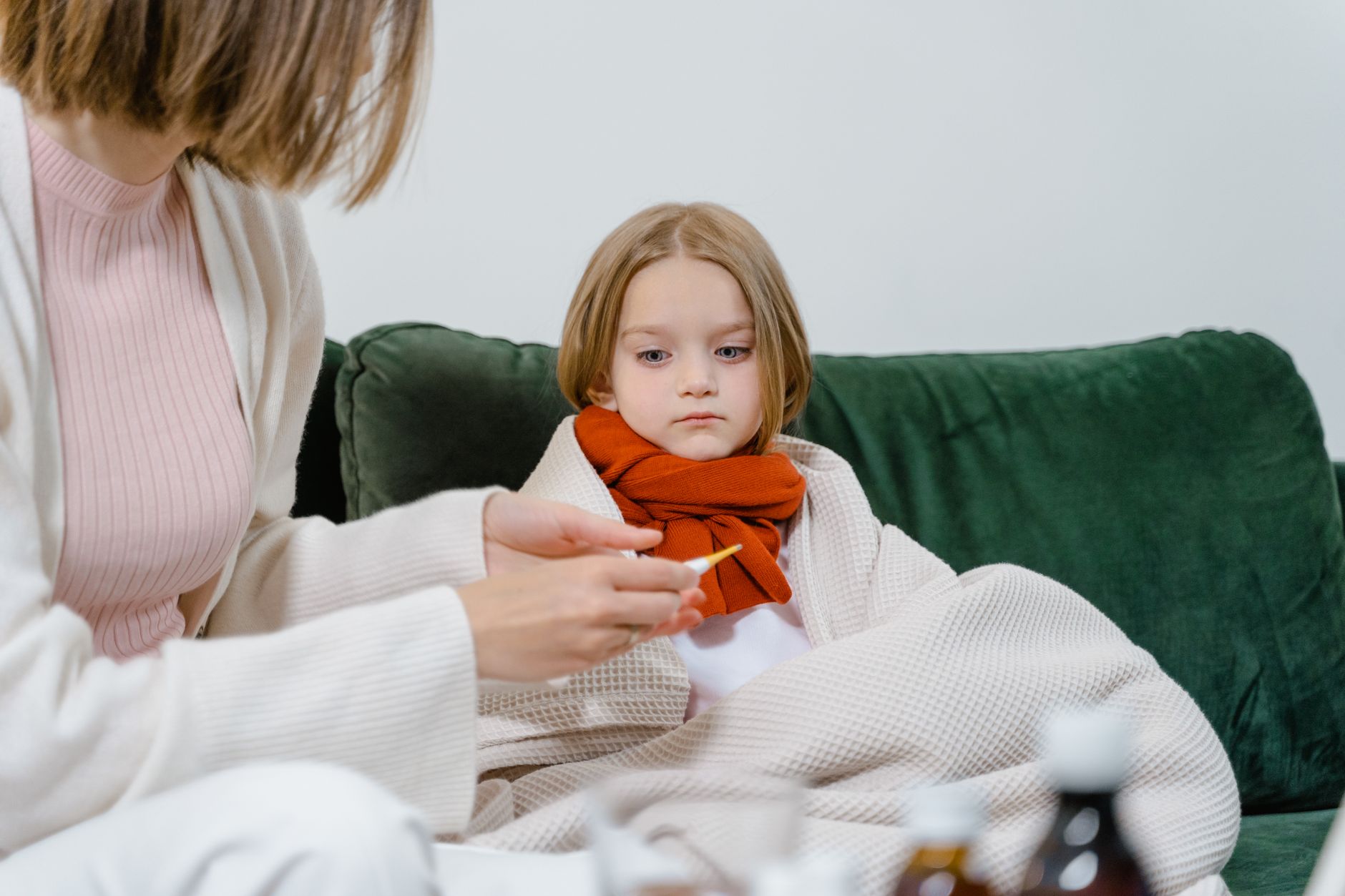Mama mierzy temperaturę choremu dziecku na zielonej kanapie