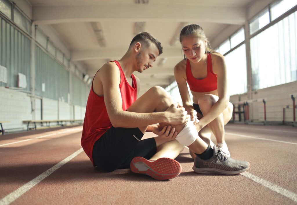 Kobieta opatruje nogę sportowca siedzącego na bieżni w hali